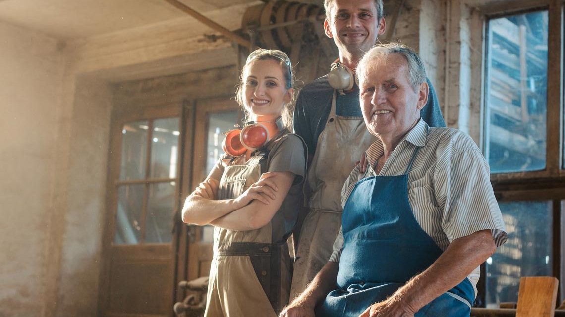Nachfolge: Generations of carpenters in their family business workshop looking at the camera