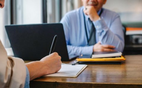 Mann sitzt am Schreibtisch und handelt Unterschied zwischen Kündigung oder Aufhebungsvertrag aus.