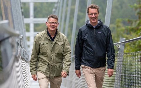 Ministerpräsidenten Rhein und Wüst gehen über Hängebrücke.