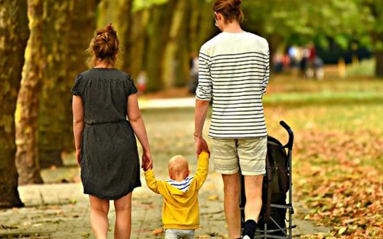 Junge Familie geht mit Kind durch den Park. Kinder betreuen, Angebhörige pflegen, Teilzeitbeschäftigung. Pflegeeltern