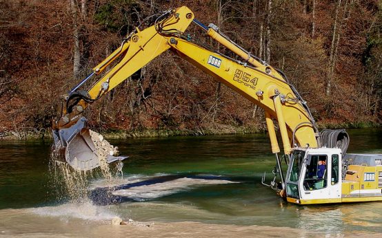 Bagger steht im Wasser und baggert Flussbett aus.