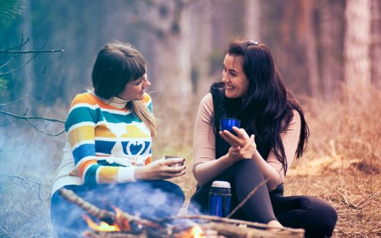 Sommercamp: Zwei Frauen sitzen an einem Lagerfeuer in der Natur.